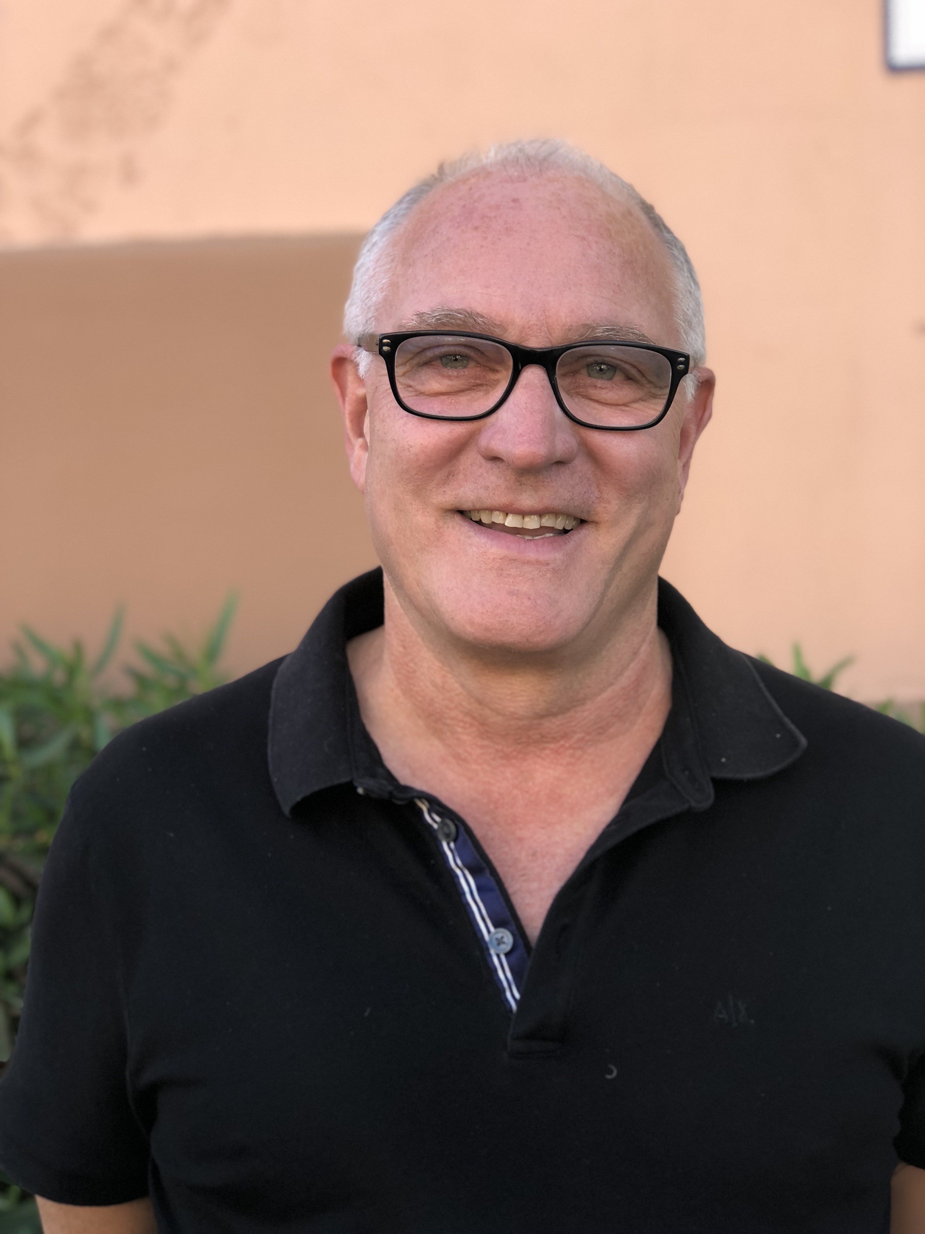 Headshot of Larry Pellegrini, smiling, in a black polo shirt outdoors