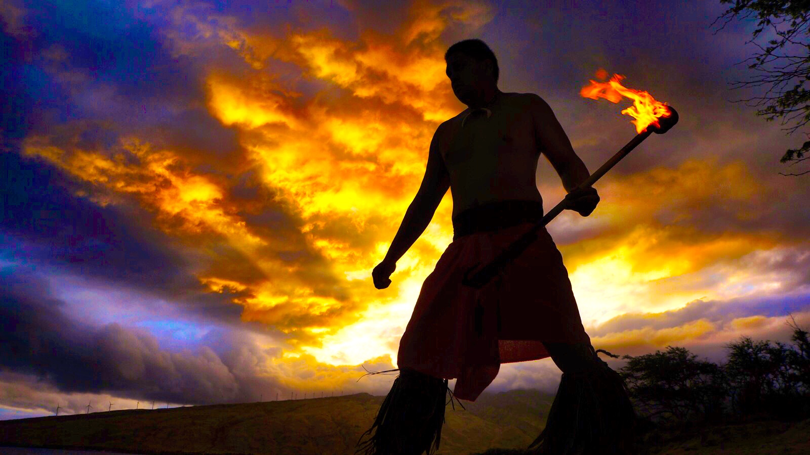A fireknife dancer silhouetted against a burning orange sunset sky