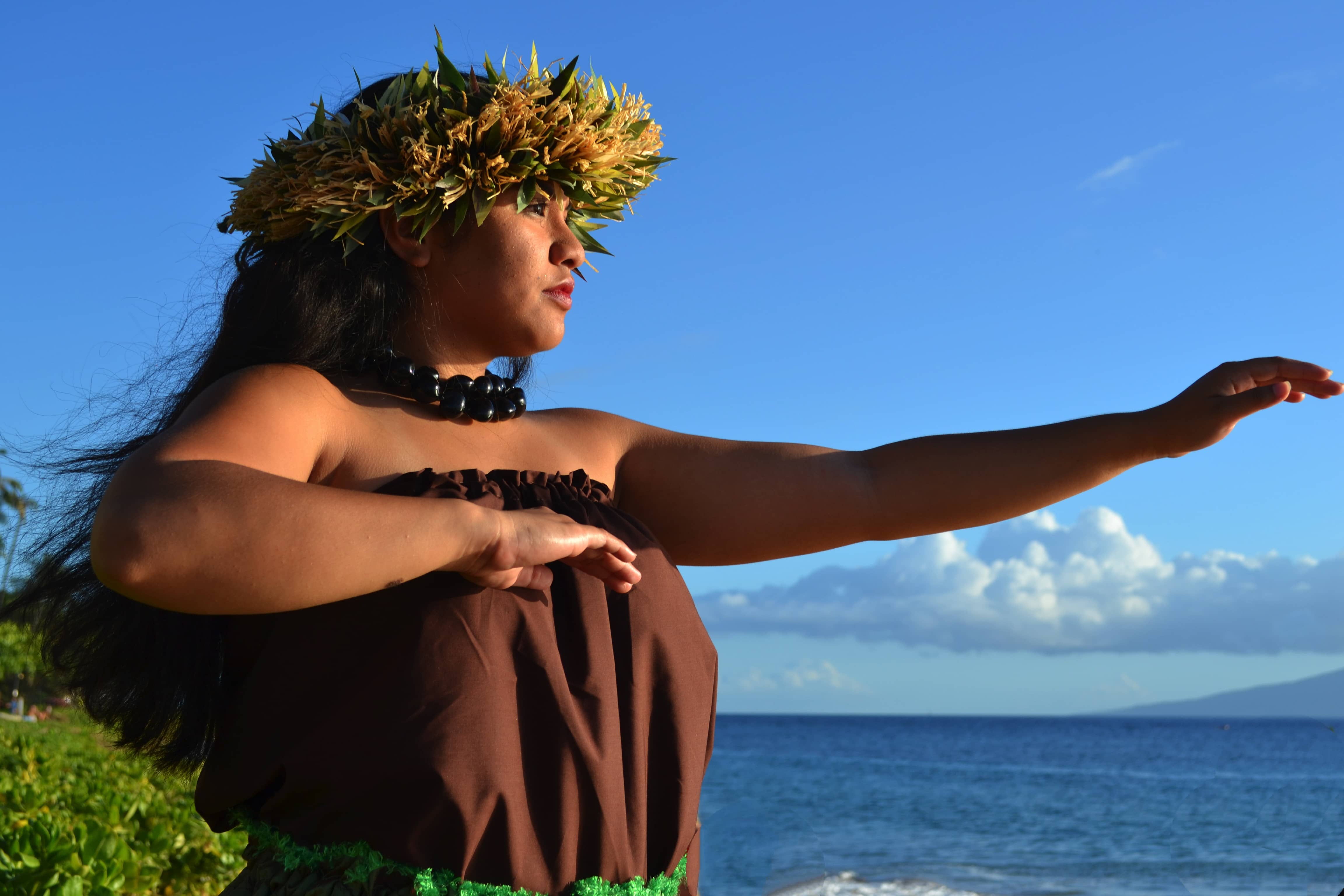 Melody Masoe dancing hula in a haku lei, one arm extended toward the ocean